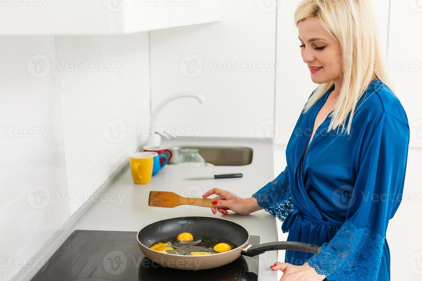 mujer joven cocinando en una cocina nueva haciendo huevos revueltos para el desayuno foto