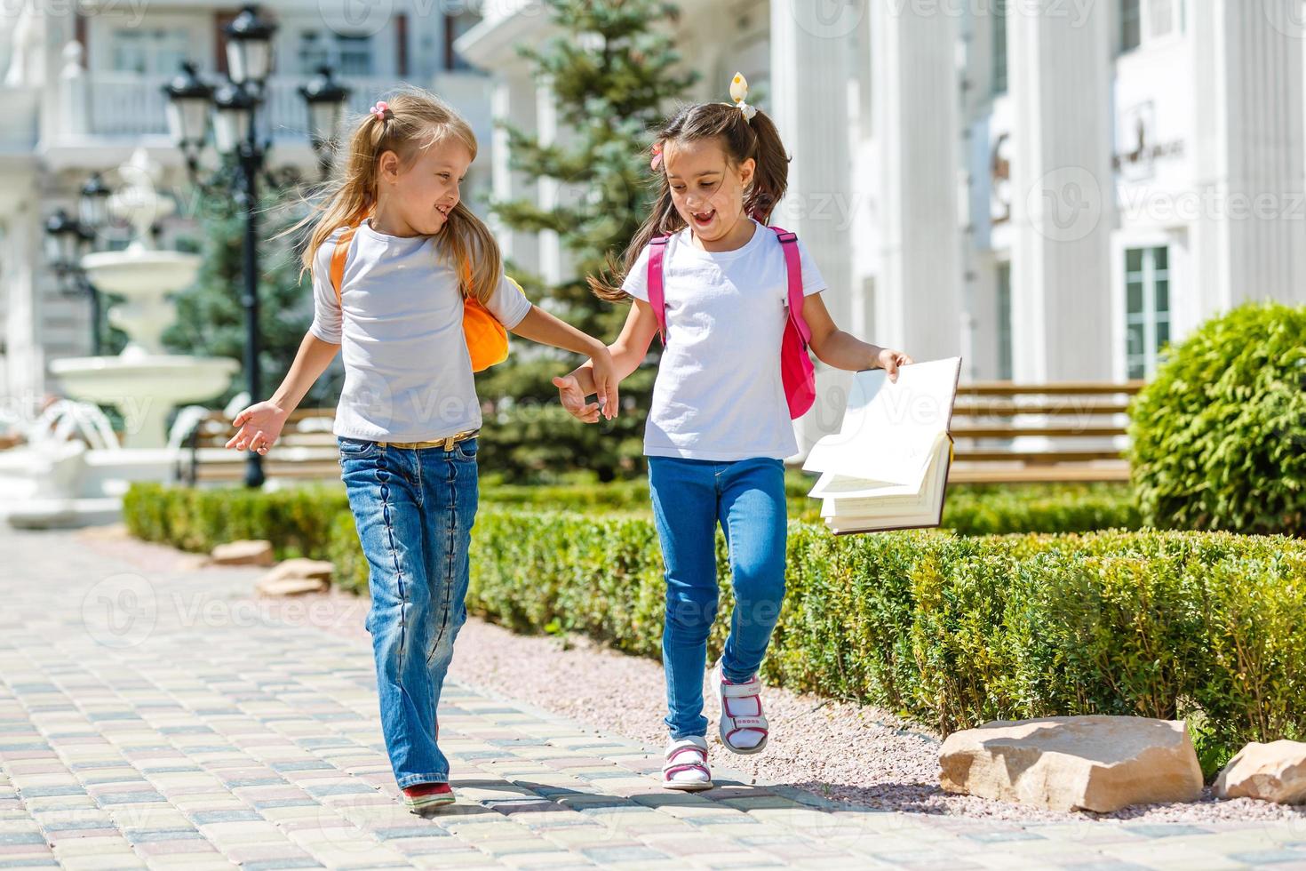 two school girls wearing backpack outside the primary school. schoolgirl, elementary school student going from school, graduation, summer holidays. photo