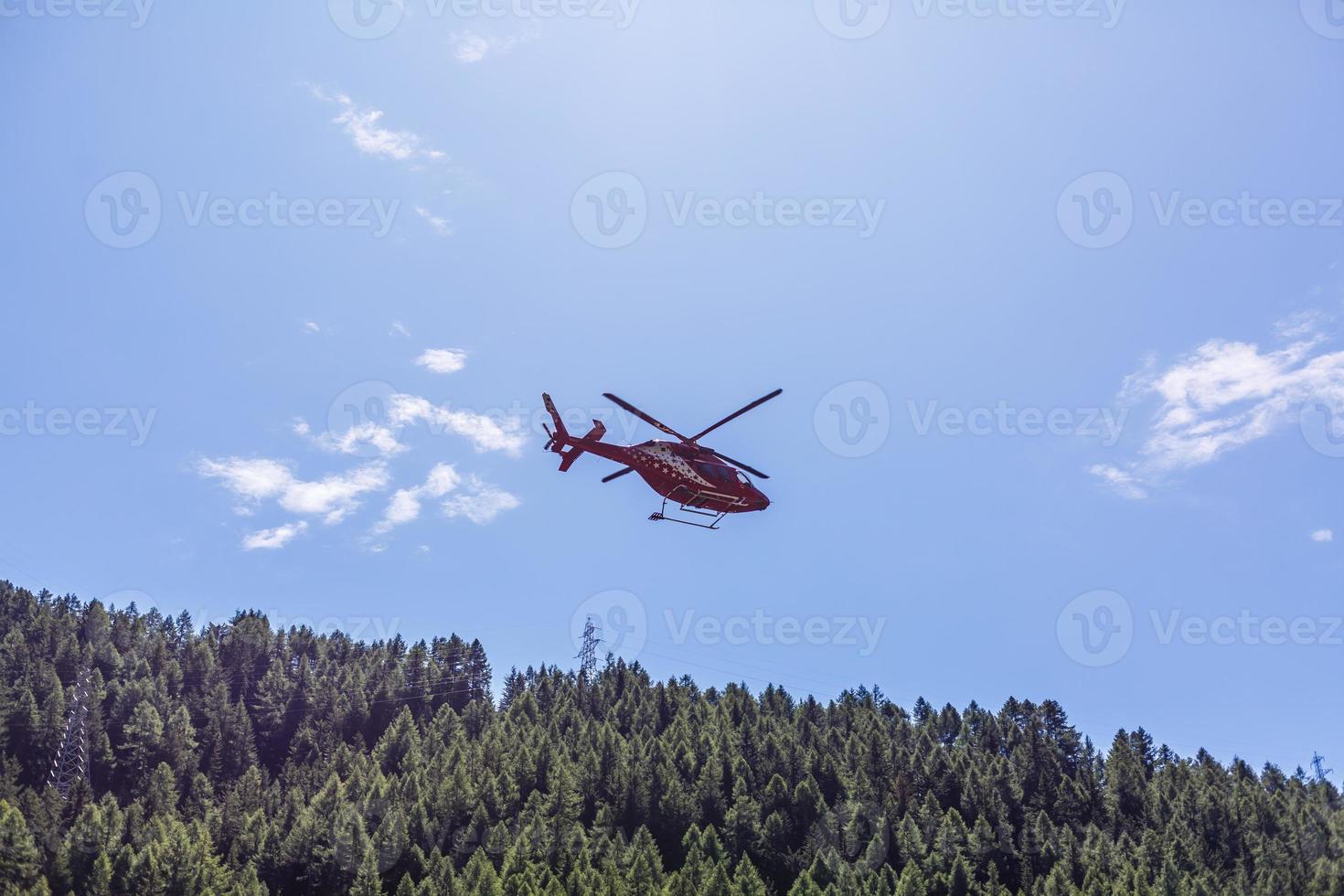 red helicopter flying over the alps photo