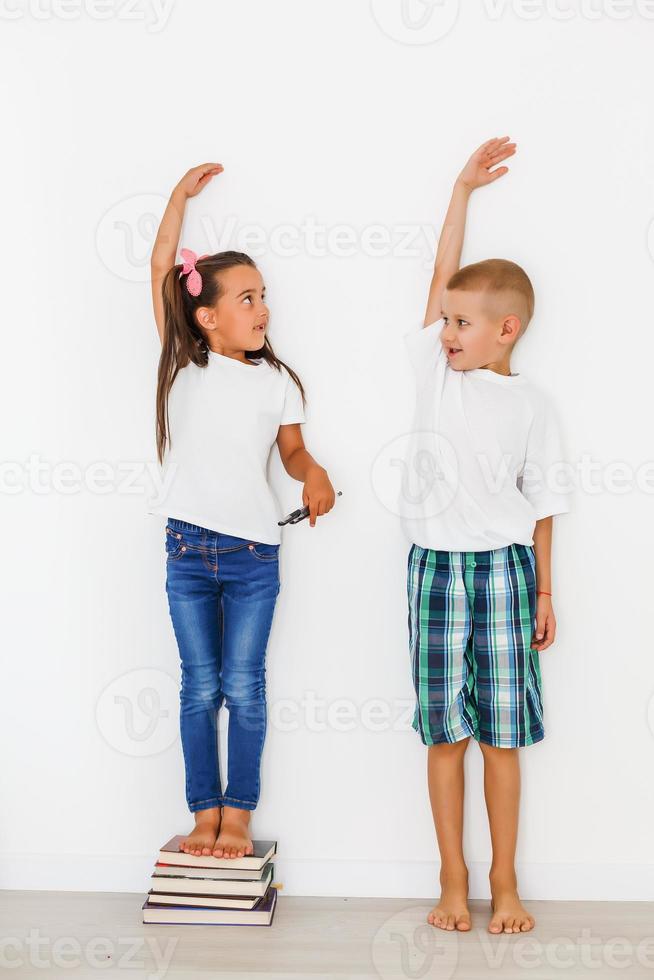 Little boy and girl measuring their height isolated on white background photo