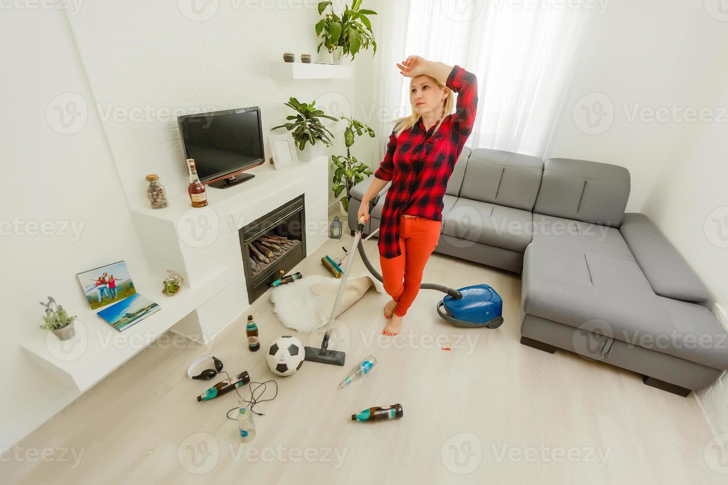 Young woman tired of spring cleaning house, washing floor with vacuum cleaner in messy room, copy space photo