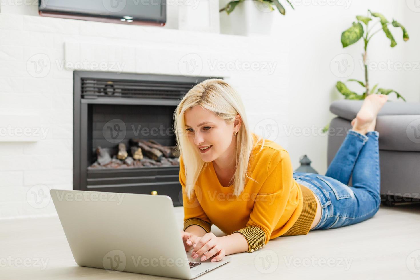 Smiling young female lying on the floor in the living room student studying at home working with her laptop computer and class notes photo