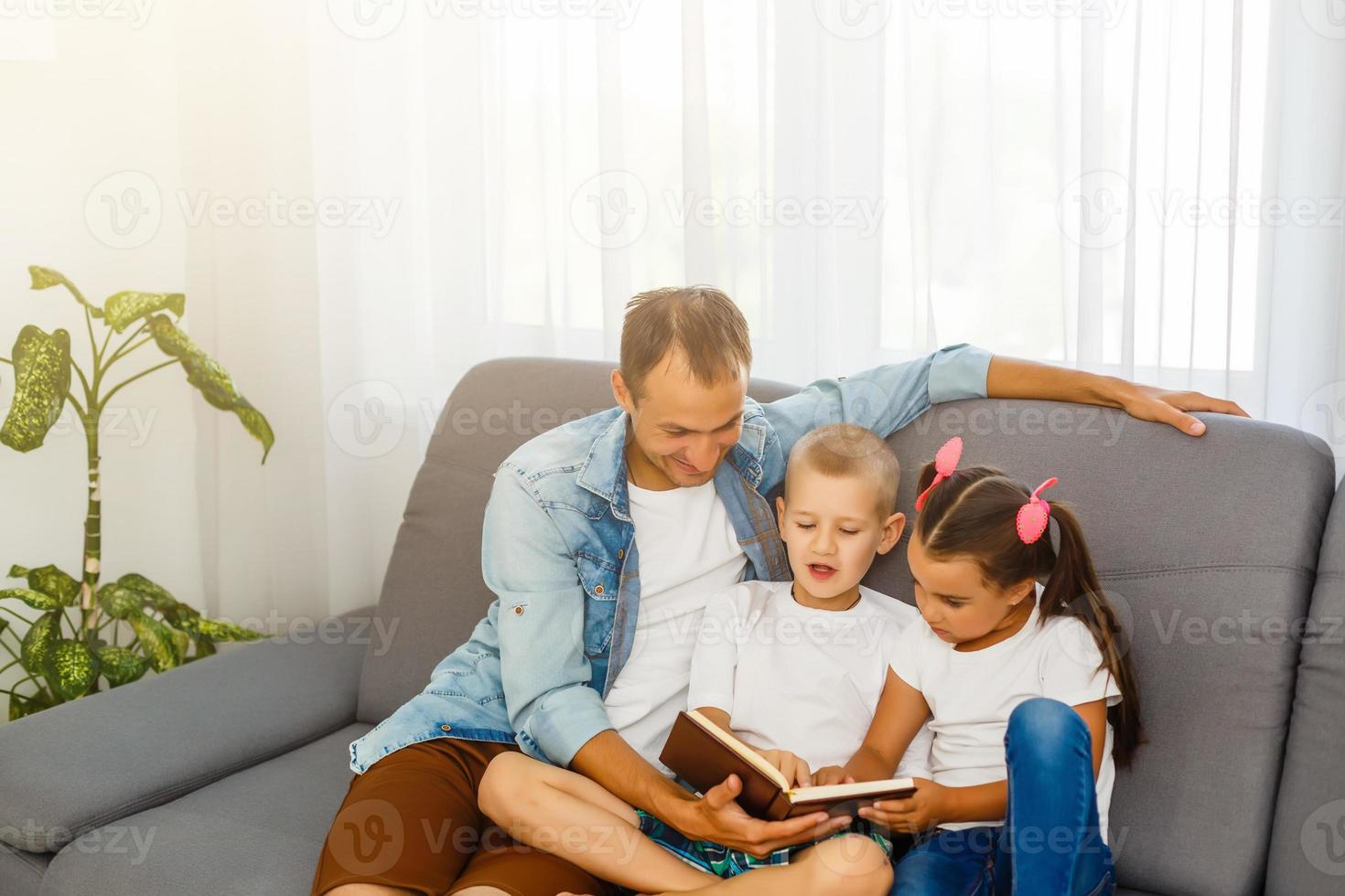 padre joven leyendo un libro para niños pequeños foto