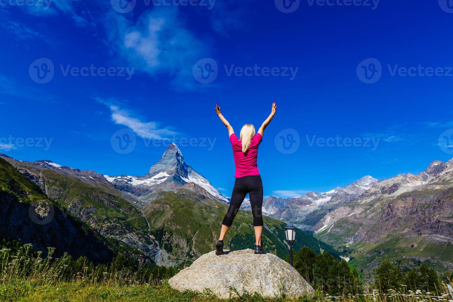 Young girl holds hands up against the sky and mountain photo