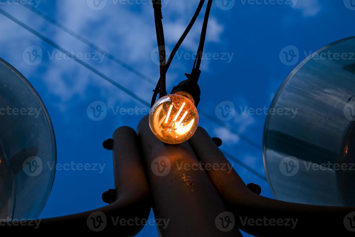 Close up of an Edison-style filament on a light bulb against a cloudy sky. Energy crisis. photo