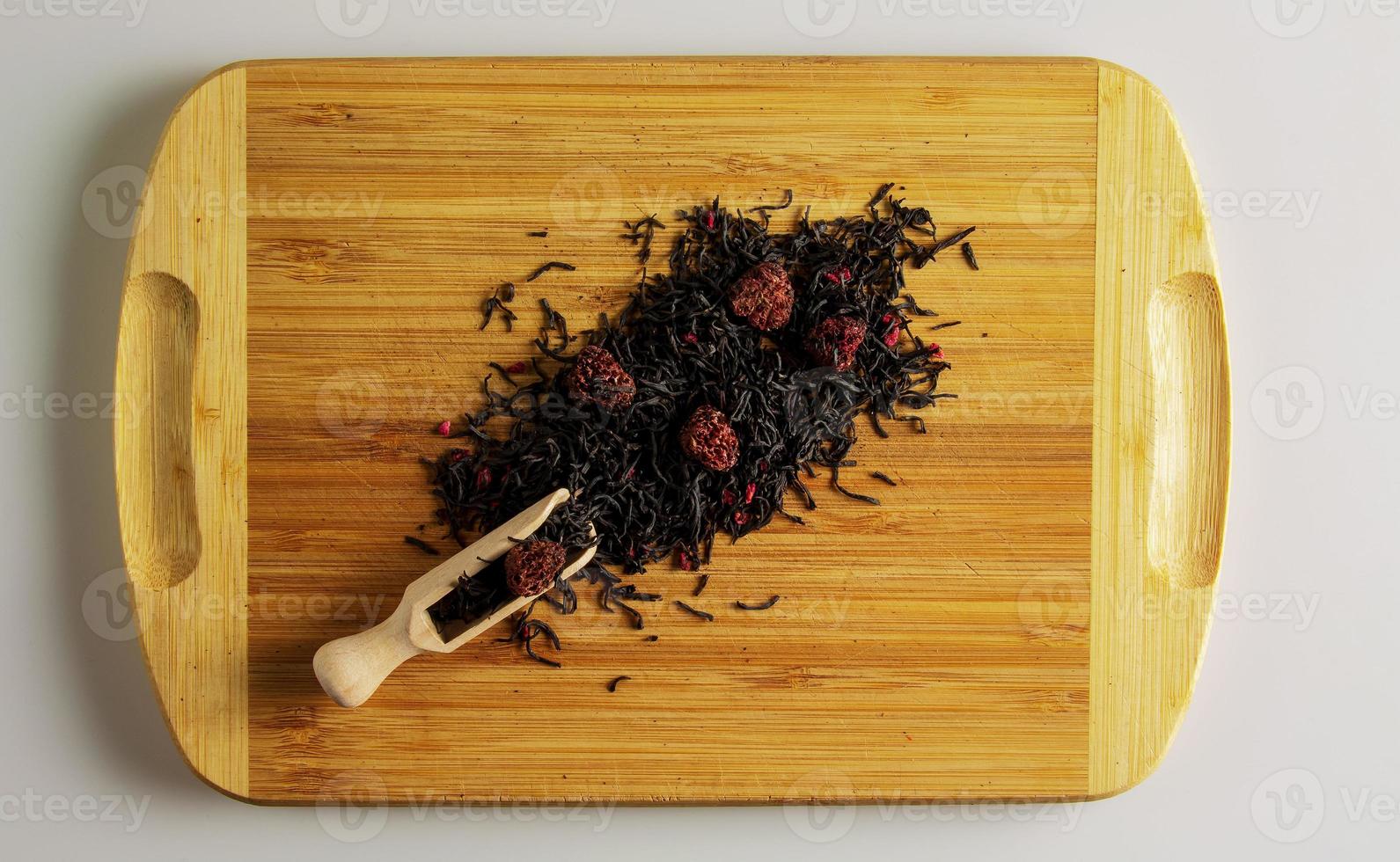 Background of dry tea based on black with whole raspberries on a wooden background. photo