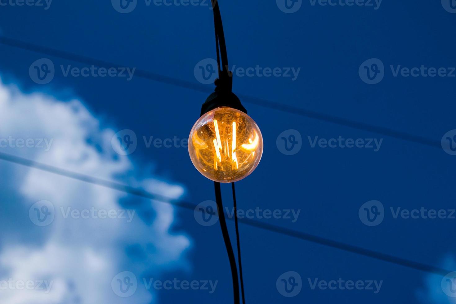 Close up of an Edison-style filament on a light bulb against a cloudy sky. Energy crisis. photo