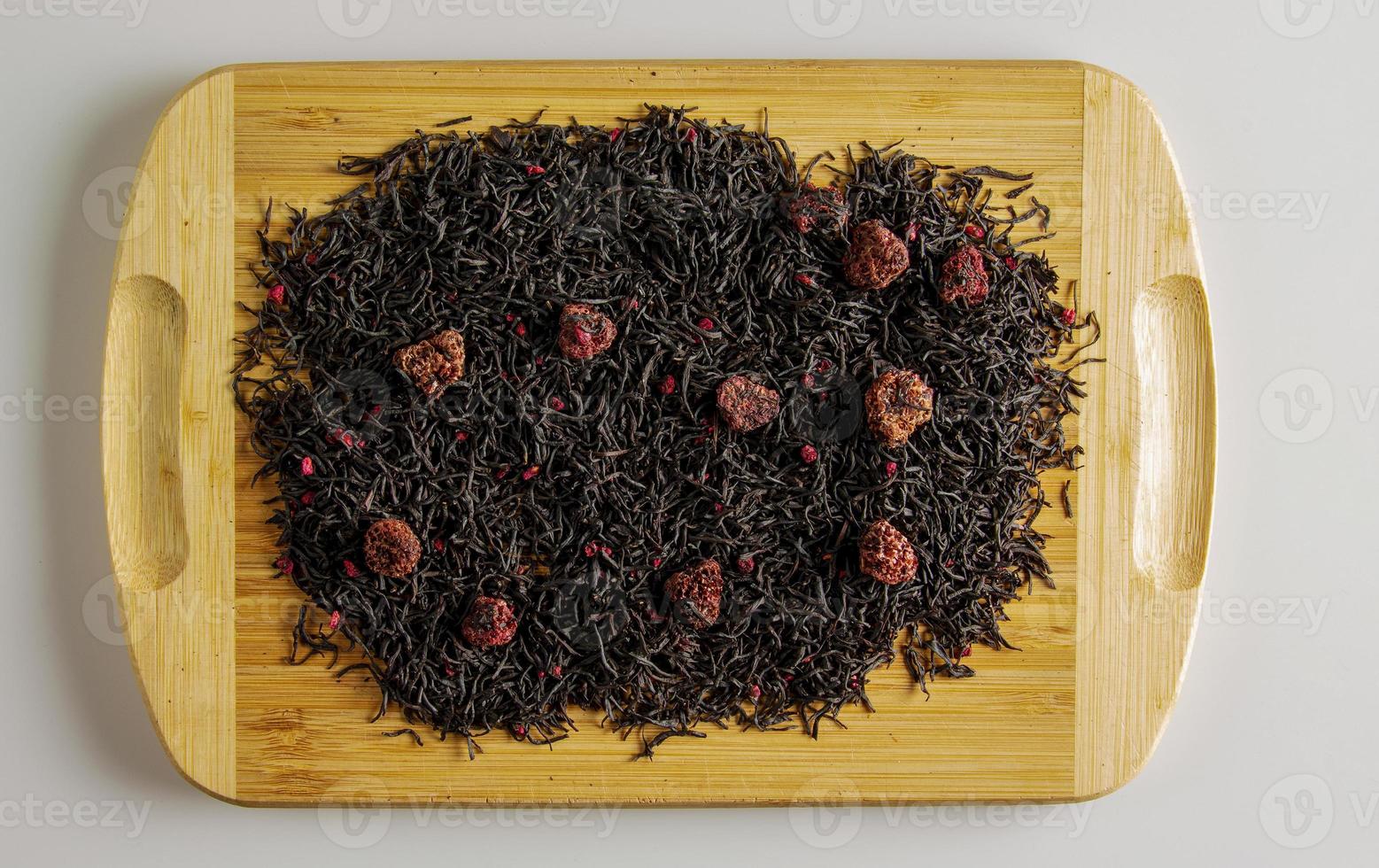 Background of dry tea based on black with whole raspberries on a wooden background. photo