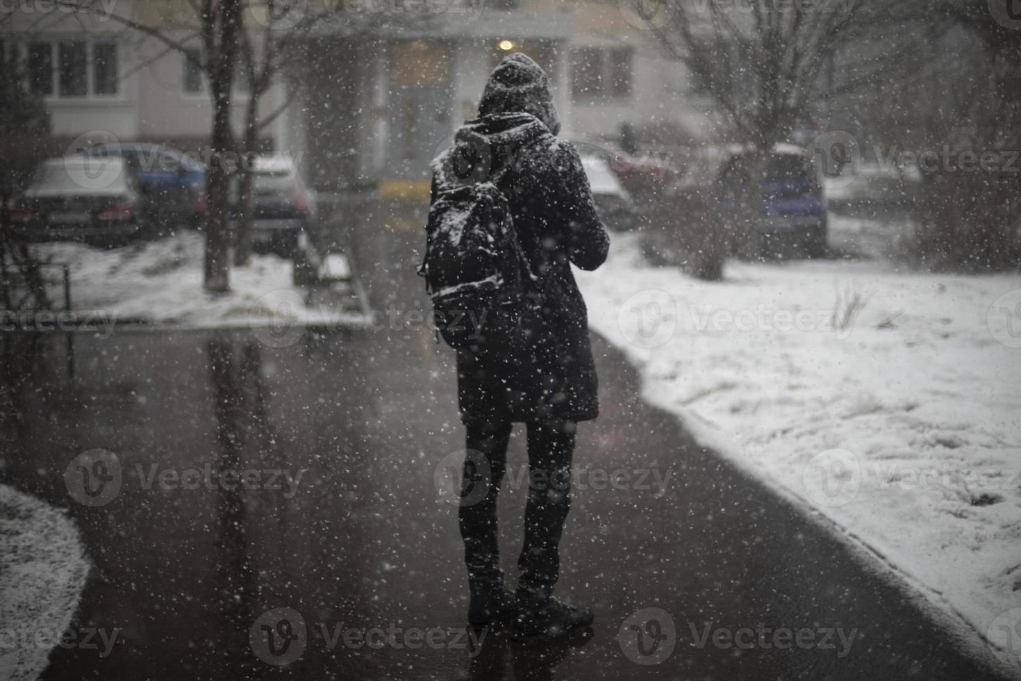 hombre afuera en nevadas. ropa negra en la nieve. chico está parado en medio de la ciudad. foto