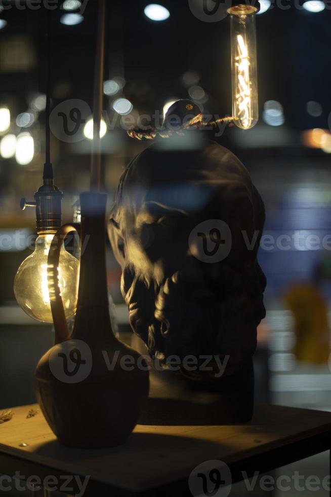 Sculpture of head with lamps. Jug on table. Incandescent lamps in interior. photo