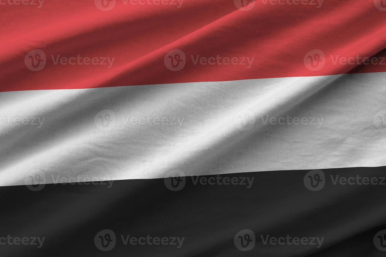 Yemen flag with big folds waving close up under the studio light indoors. The official symbols and colors in banner photo
