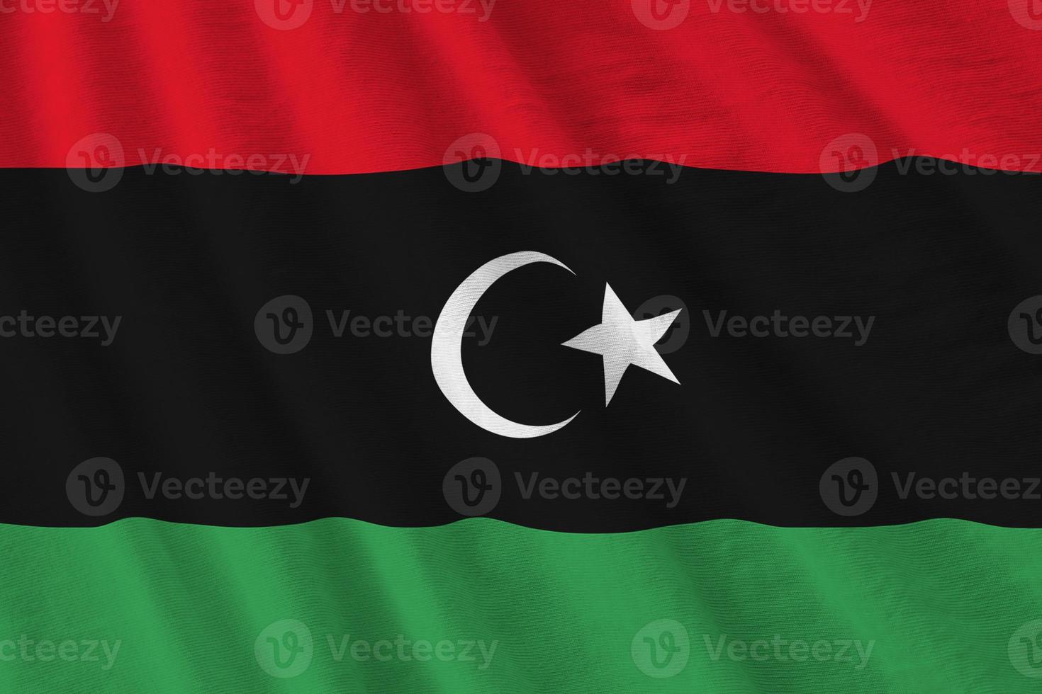 Libya flag with big folds waving close up under the studio light indoors. The official symbols and colors in banner photo