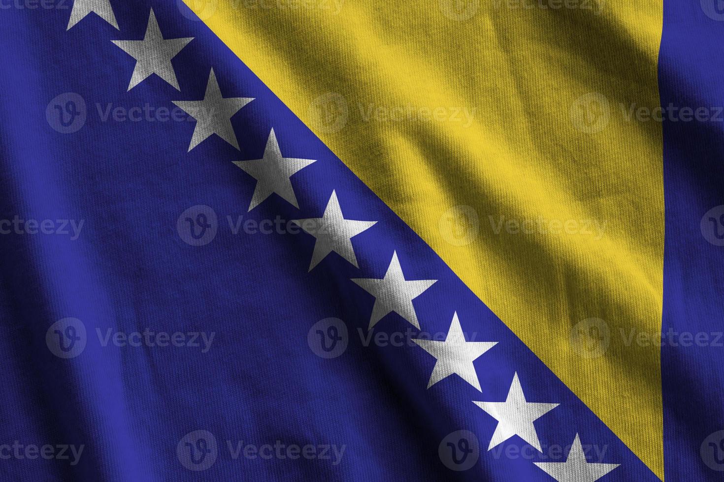 Bosnia and Herzegovina flag with big folds waving close up under the studio light indoors. The official symbols and colors in banner photo