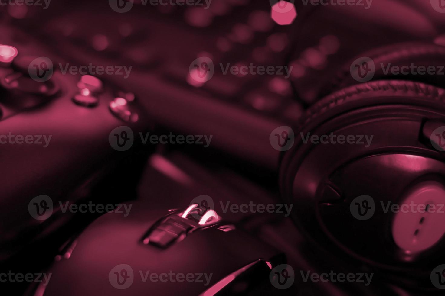 Modern gamepad and gaming mouse lies with keyboard and headphones on table in dark playroom scene. Devices for playing video games at home Image toned in Viva Magenta, color of the 2023 year photo