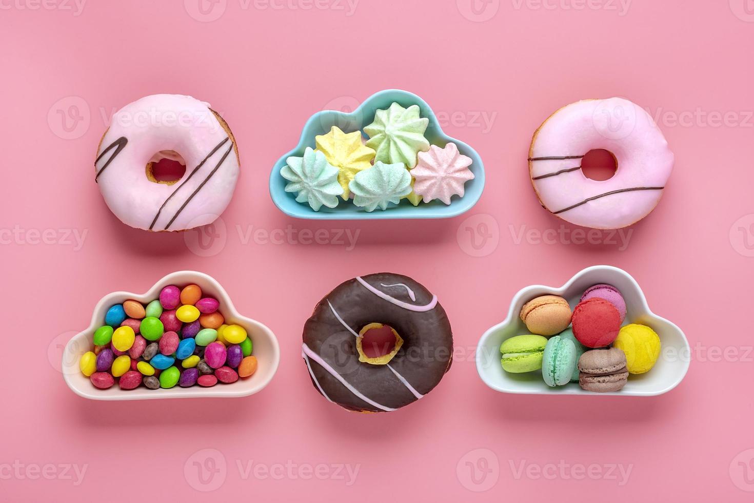 sweets and meringues in bowl in shape of cloud, chocolate with colorful topping and pink donut isolated on pink background Flat lay Top View Knolling Unhealthy and tasty food concept photo