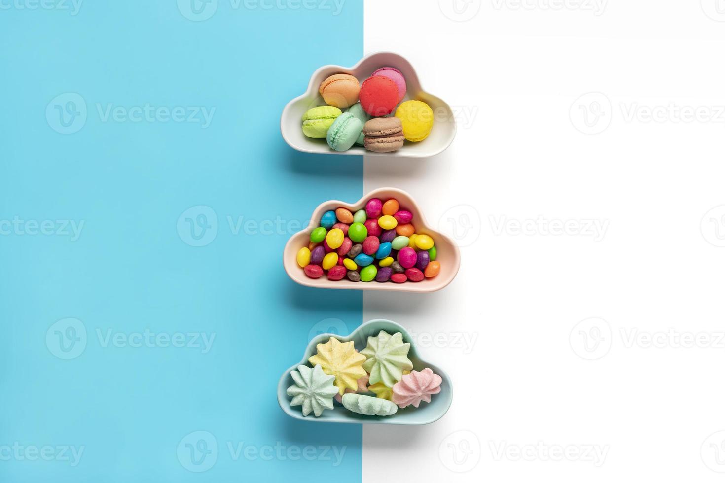 Caramelos coloridos: piruletas, merengues, macarrones en un tazón en forma de nube aislado en azul, fondo blanco plano vista superior knolling comida poco saludable y sabrosa concepto creativo tarjeta de vacaciones foto