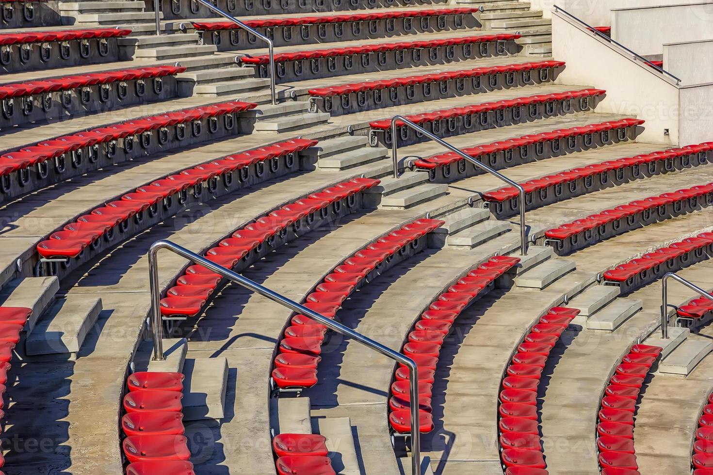 Empty red plastic chairs in the stands of the stadium or amphitheater. Many empty seats for spectators in the stands. photo
