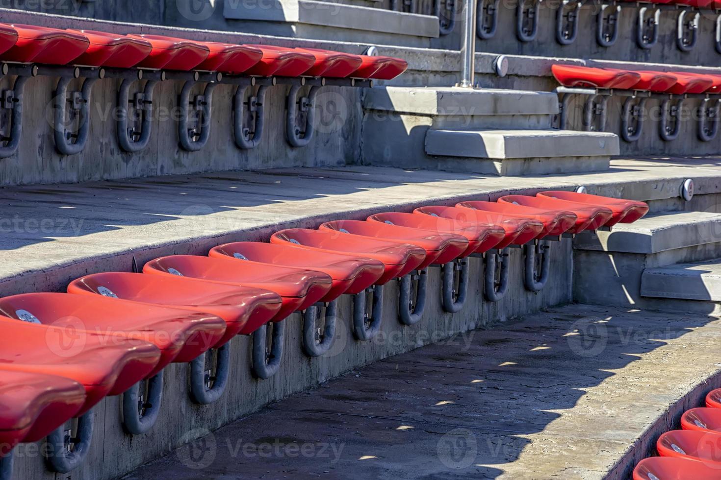 Empty red plastic chairs in the stands of the stadium or amphitheater. Many empty seats for spectators in the stands. Close photo