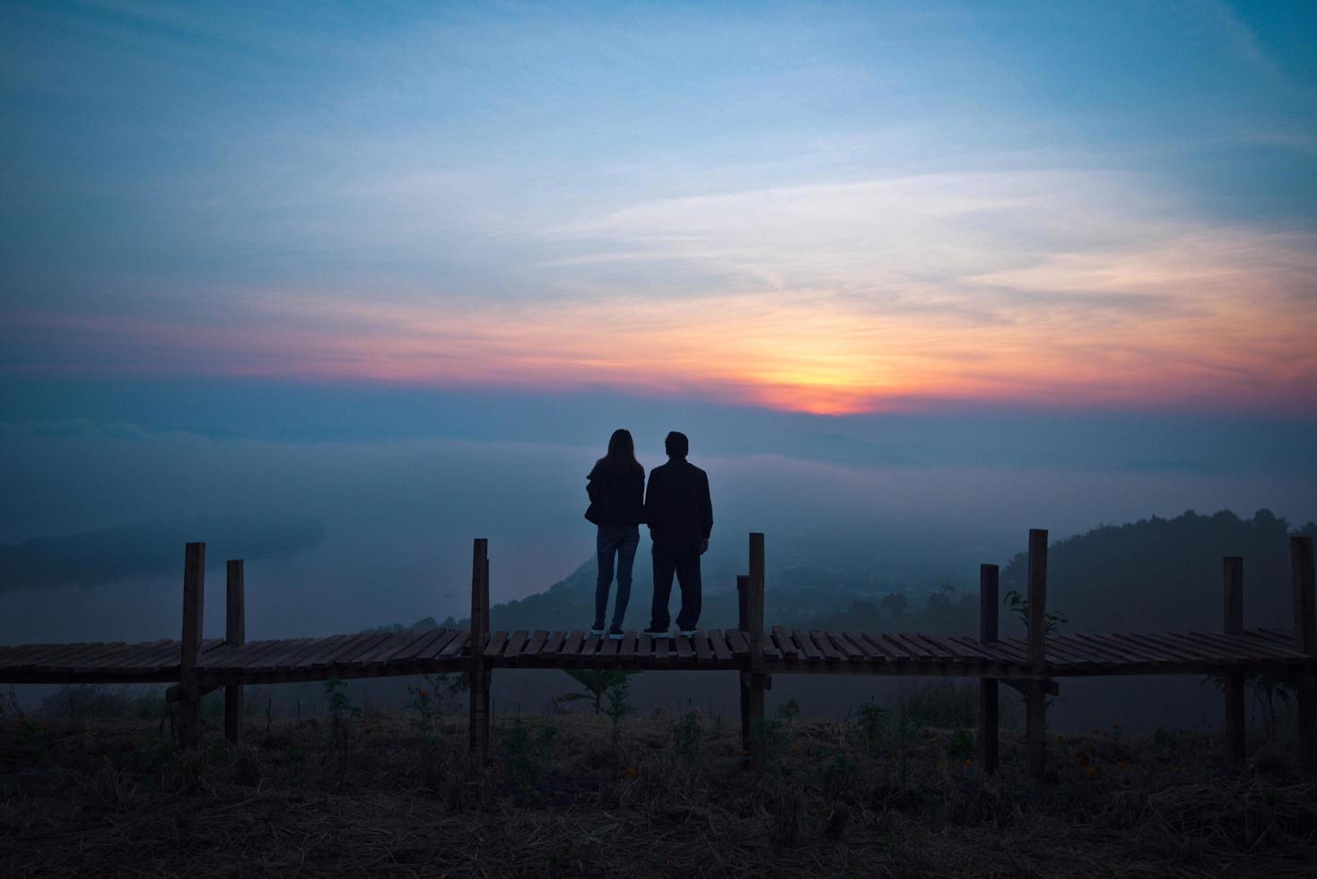 View on hill lover couple silhouette standing on a wooden bridge photo