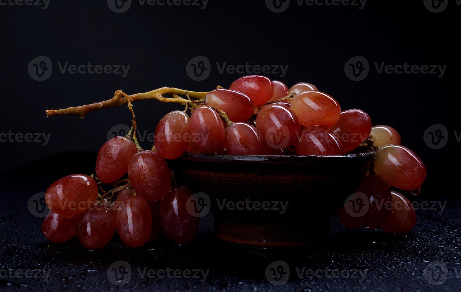 A bunch of ripe red grapes in a clay plate, on a dark background. photo