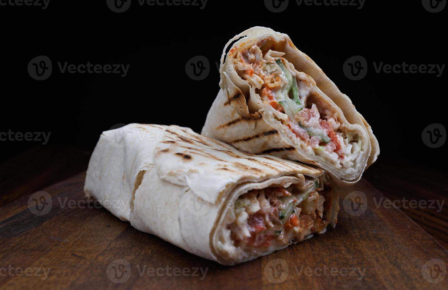 Delicious shawarma with juicy delicious filling lies on a wooden board. photo
