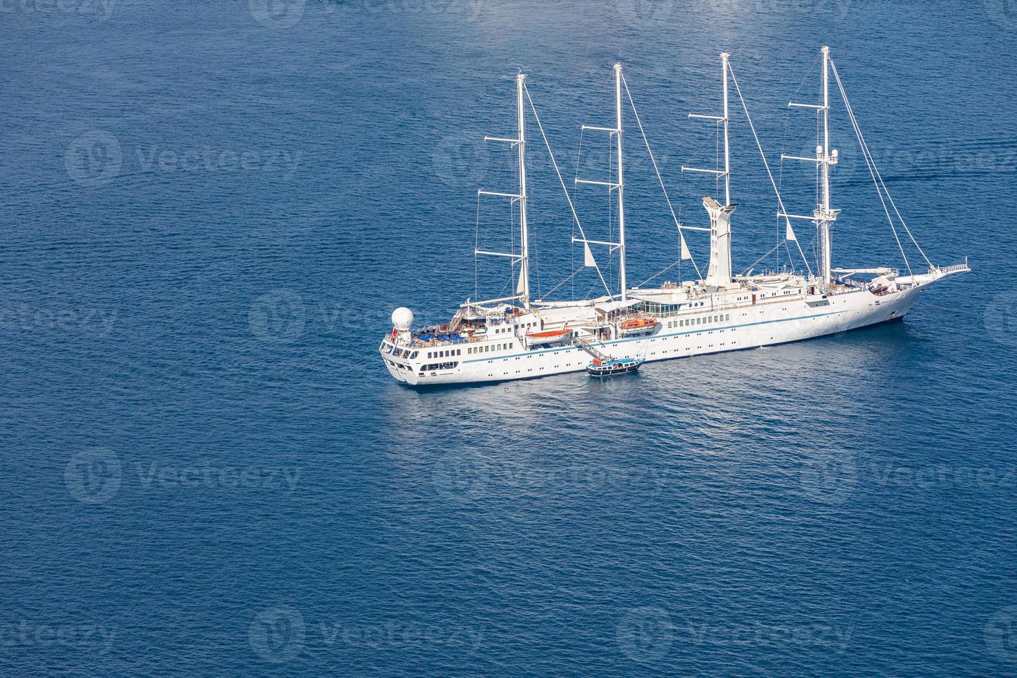 Beautiful luxury white yacht. Aerial view of sailing boat anchoring blue sea. Bird eye view, sea transportation and luxury travel as cruise ship.People boarding in Santorini bay photo