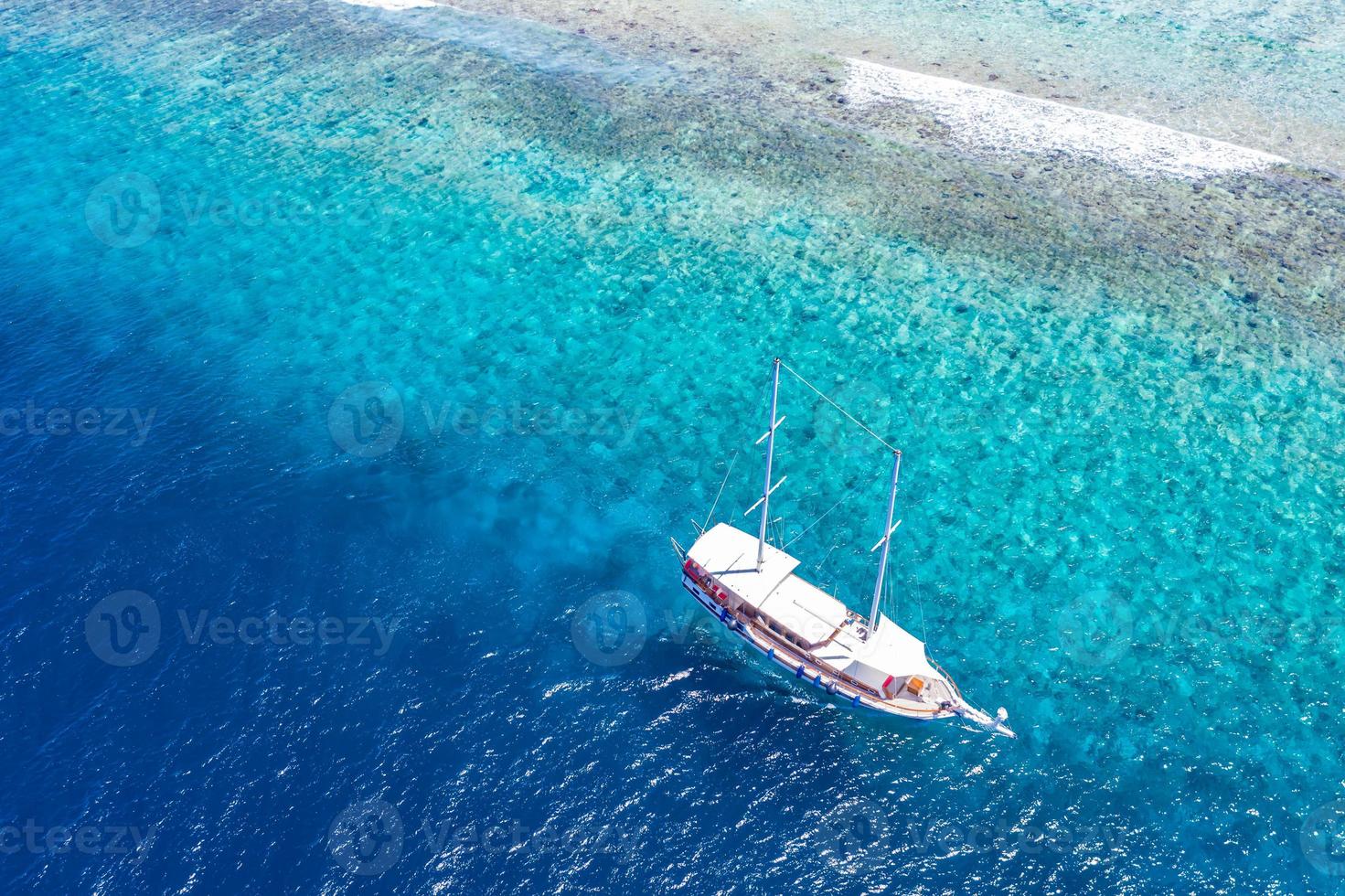 Aerial view of sailing boat anchoring on coral reef. Drone view, water sport theme. Luxury cruise and marine travel background. Beautiful nature scenery, sea ocean water concept. Maldives aerial photo
