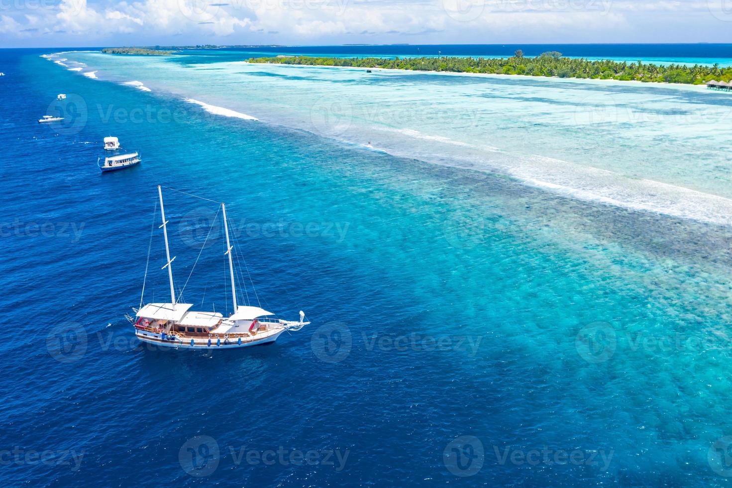 Aerial view of sailing boat anchoring on coral reef. Drone view, water sport theme. Luxury cruise and marine travel background. Beautiful nature scenery, sea ocean water concept. Maldives aerial photo