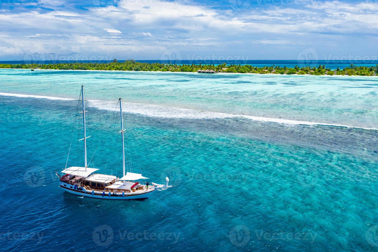 Aerial view of sailing boat anchoring on coral reef. Drone view, water sport theme. Luxury cruise and marine travel background. Beautiful nature scenery, sea ocean water concept. Maldives aerial photo