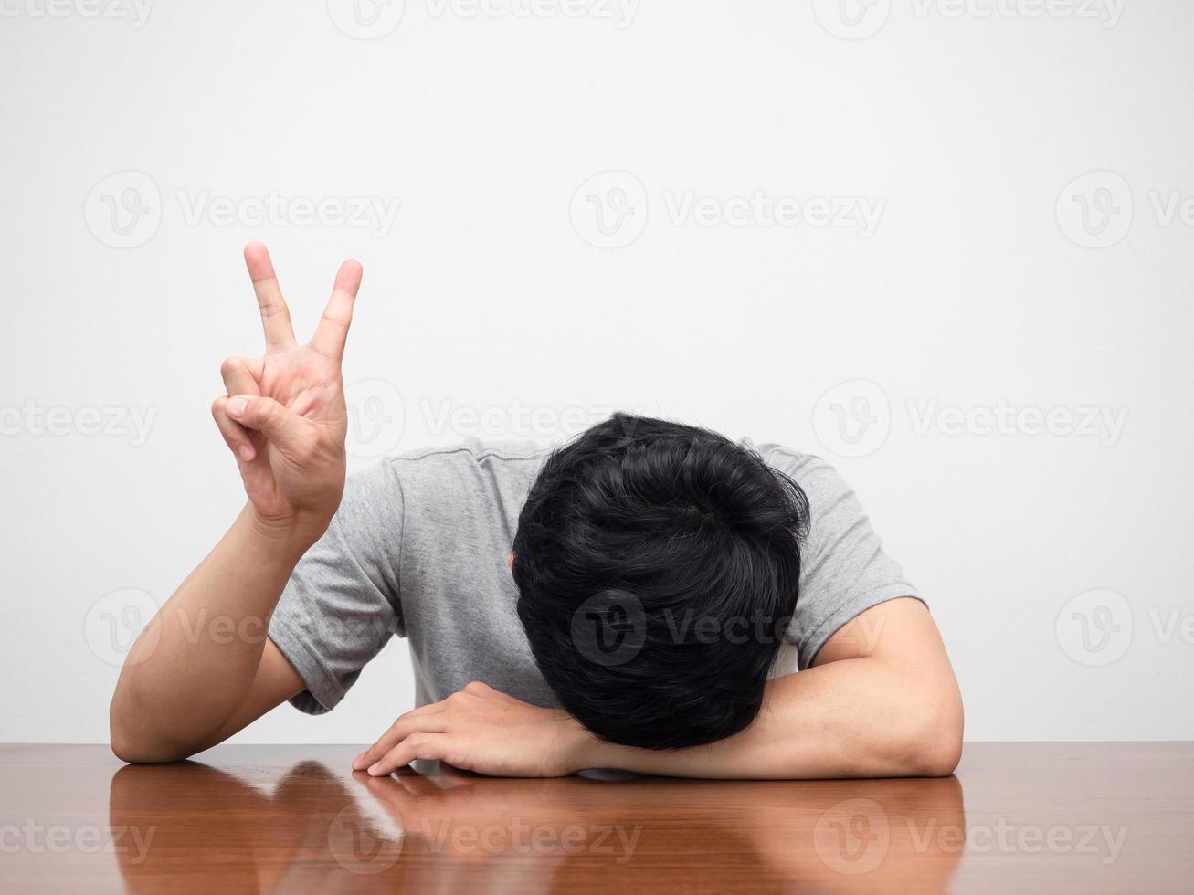 Sad man tried from working head down on table show two finger for