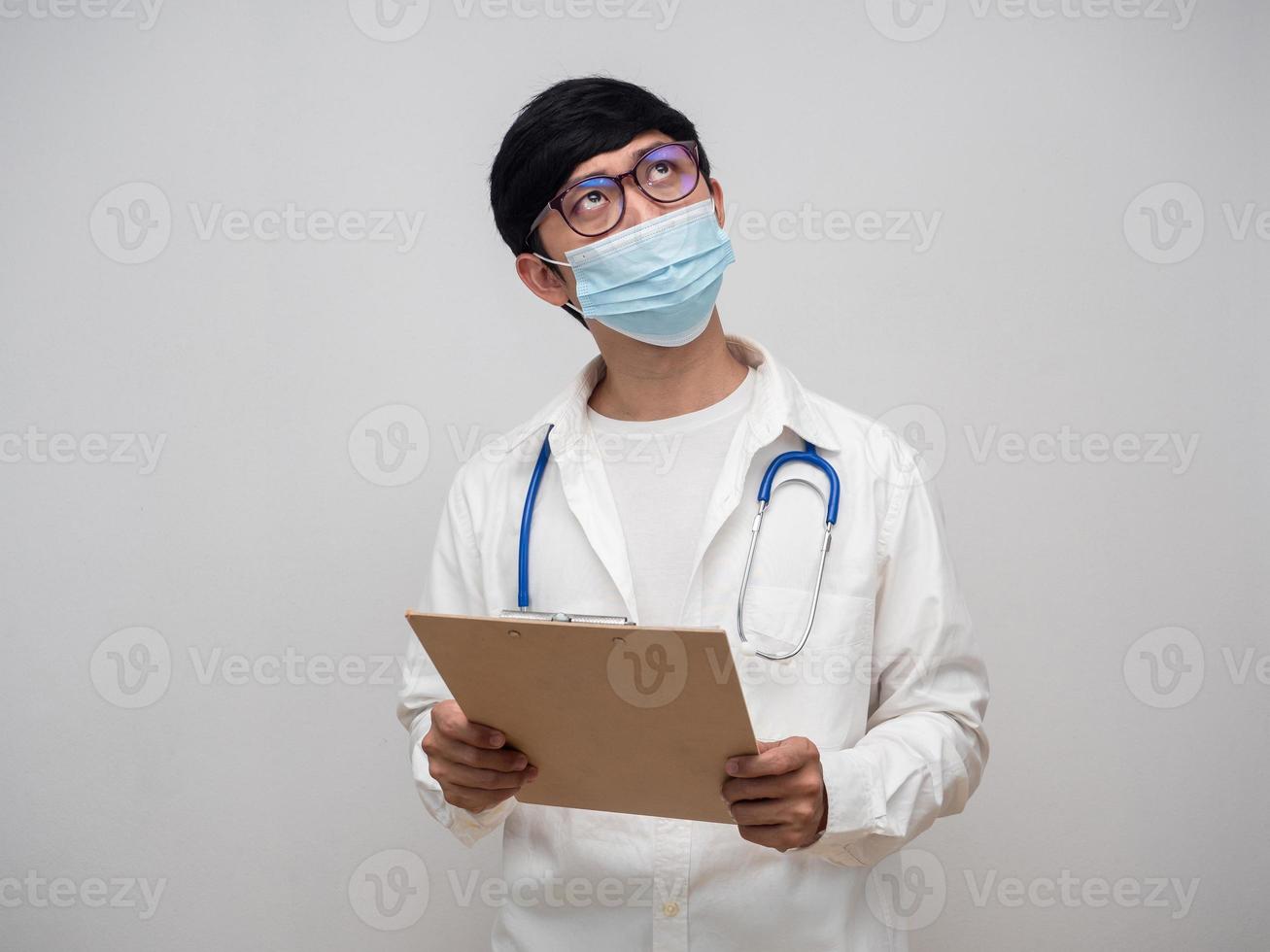 Doctor wearing medical mask hold check list board looking above white background photo