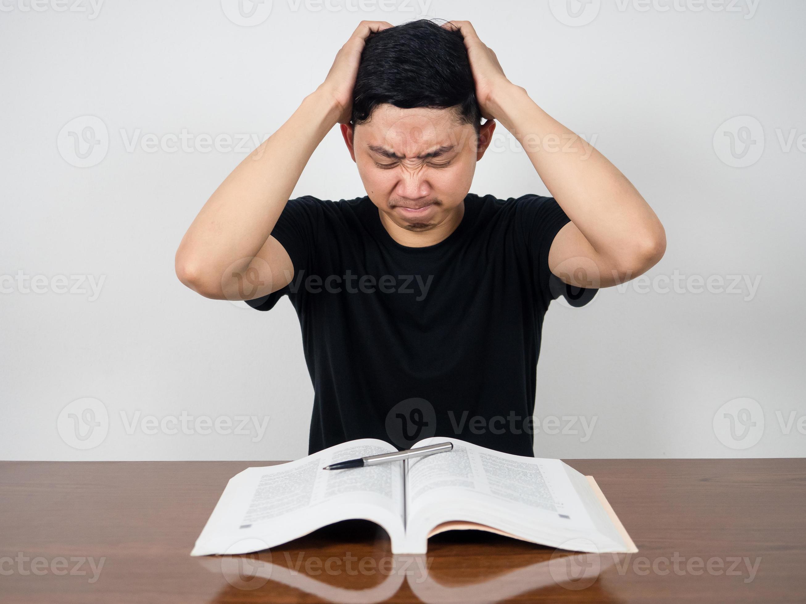 Young man hold his head feels headache with reading book on the table