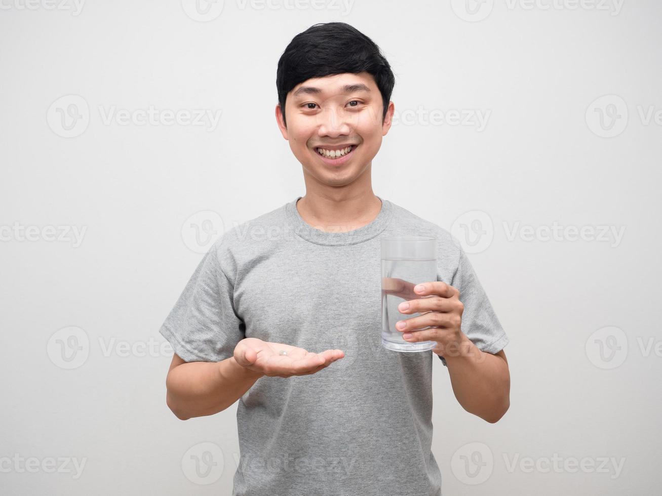 hombre joven positivo que sostiene la medicina con un vaso de agua sonrisa suave aislado foto