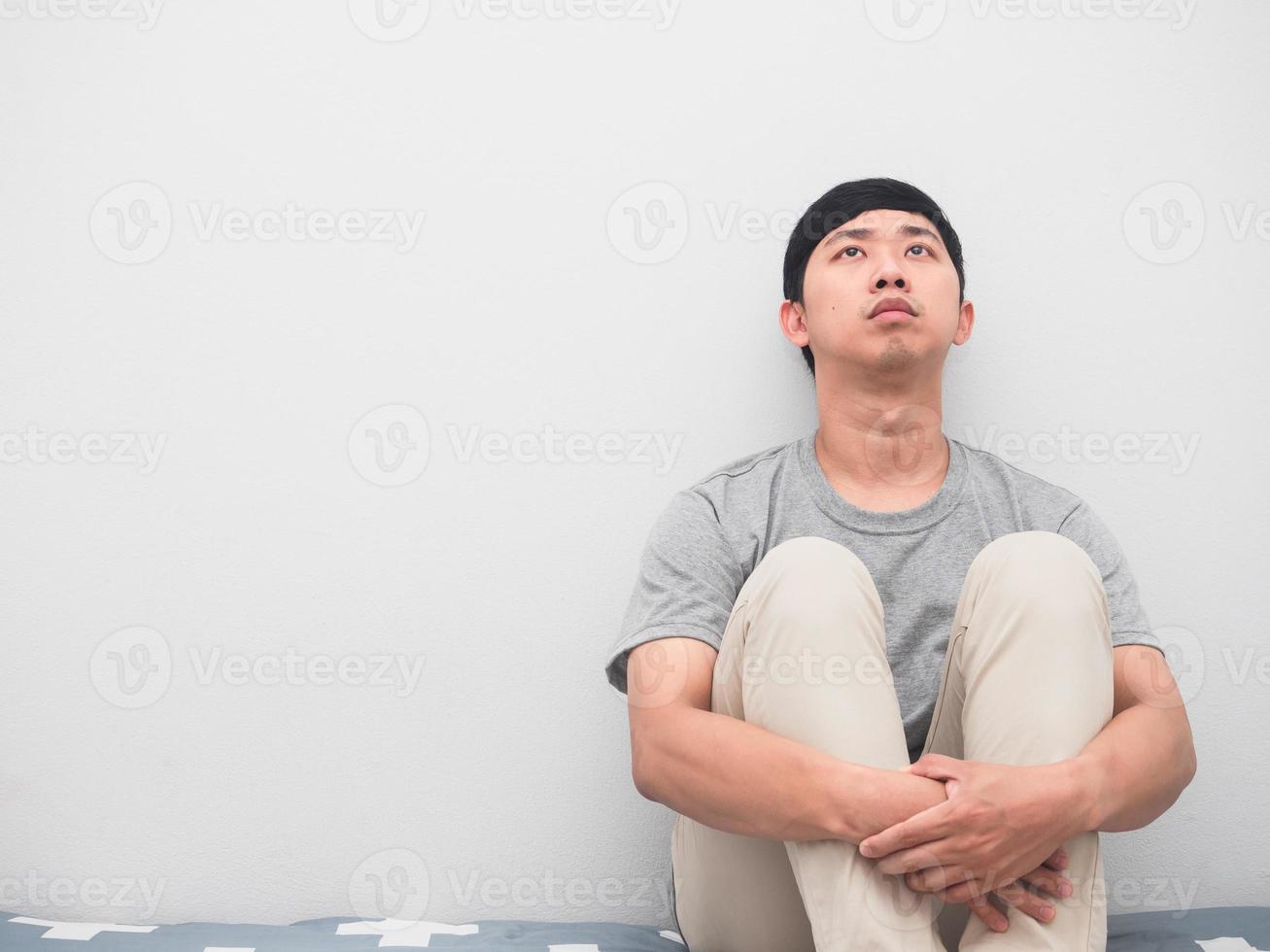 el hombre se sienta en la cama abrazando la rodilla pensativa tristeza emoción mirando hacia arriba foto