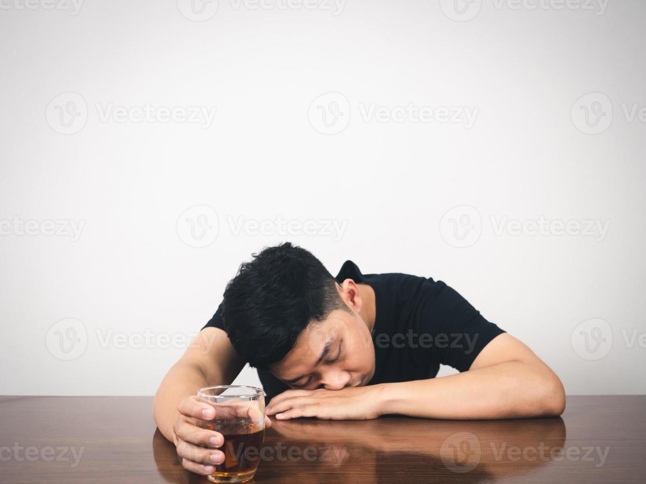 Alcoholism man hangover laying at table and hold alcohol glass in hand photo