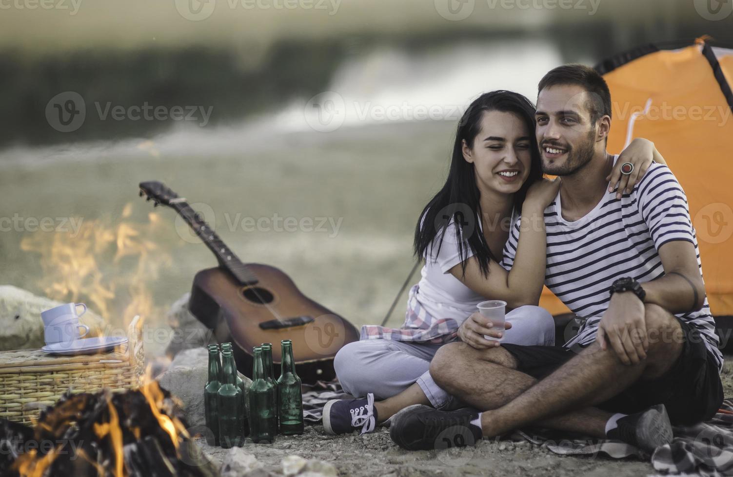 Picnic holiday concept. Beautiful couple having fun making BBQ on bonfire and relaxing by a lake. photo