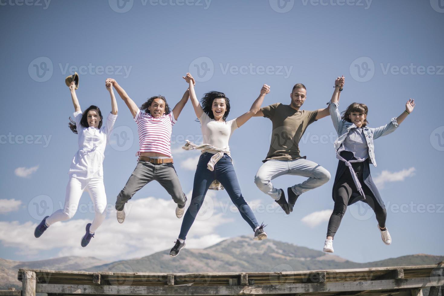 Portrait of young friends jumping from jetty into lake. Friends in mid air on a sunny day at the lake. photo