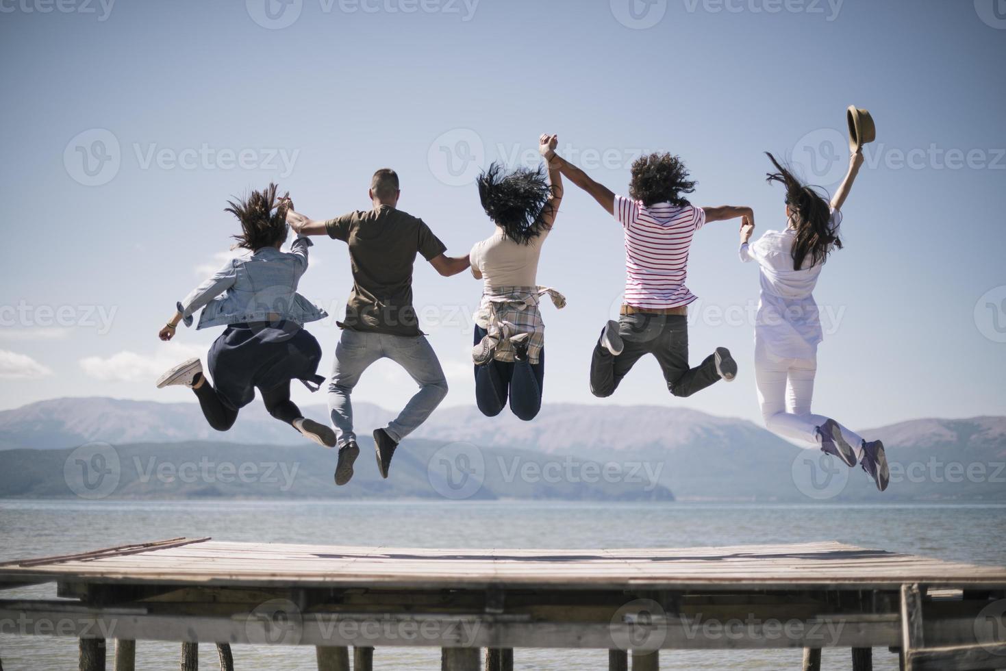Portrait of young friends jumping from jetty into lake. Friends in mid air on a sunny day at the lake. photo