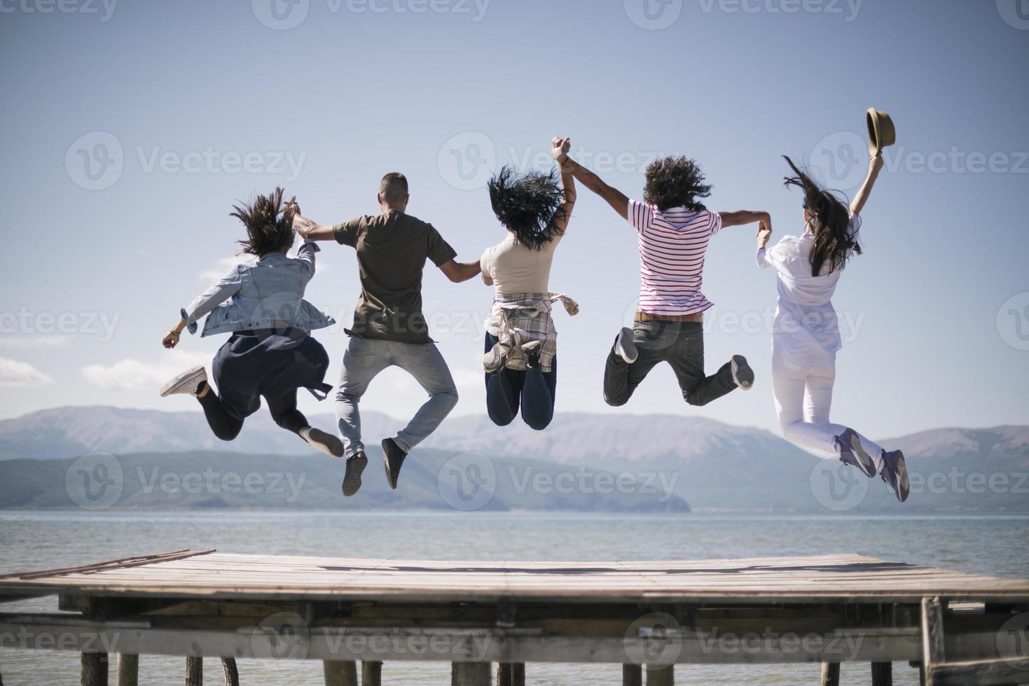 retrato de jóvenes amigos saltando del embarcadero al lago. amigos en el aire en un día soleado en el lago. foto