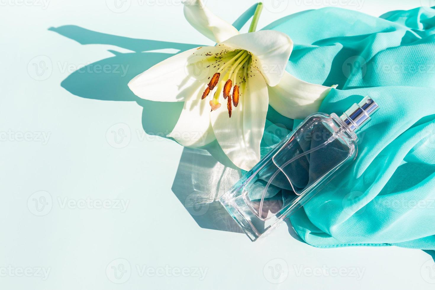 an elegant bottle of cosmetic spray or perfume against the background of a light scarf and a white lily flower. space for text. aroma presentation. photo