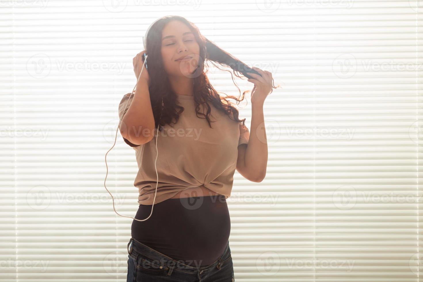 retrato de mujer embarazada cerca de la ventana en casa y escuchando música en auriculares con espacio para copiar. concepto de embarazo y ocio. foto