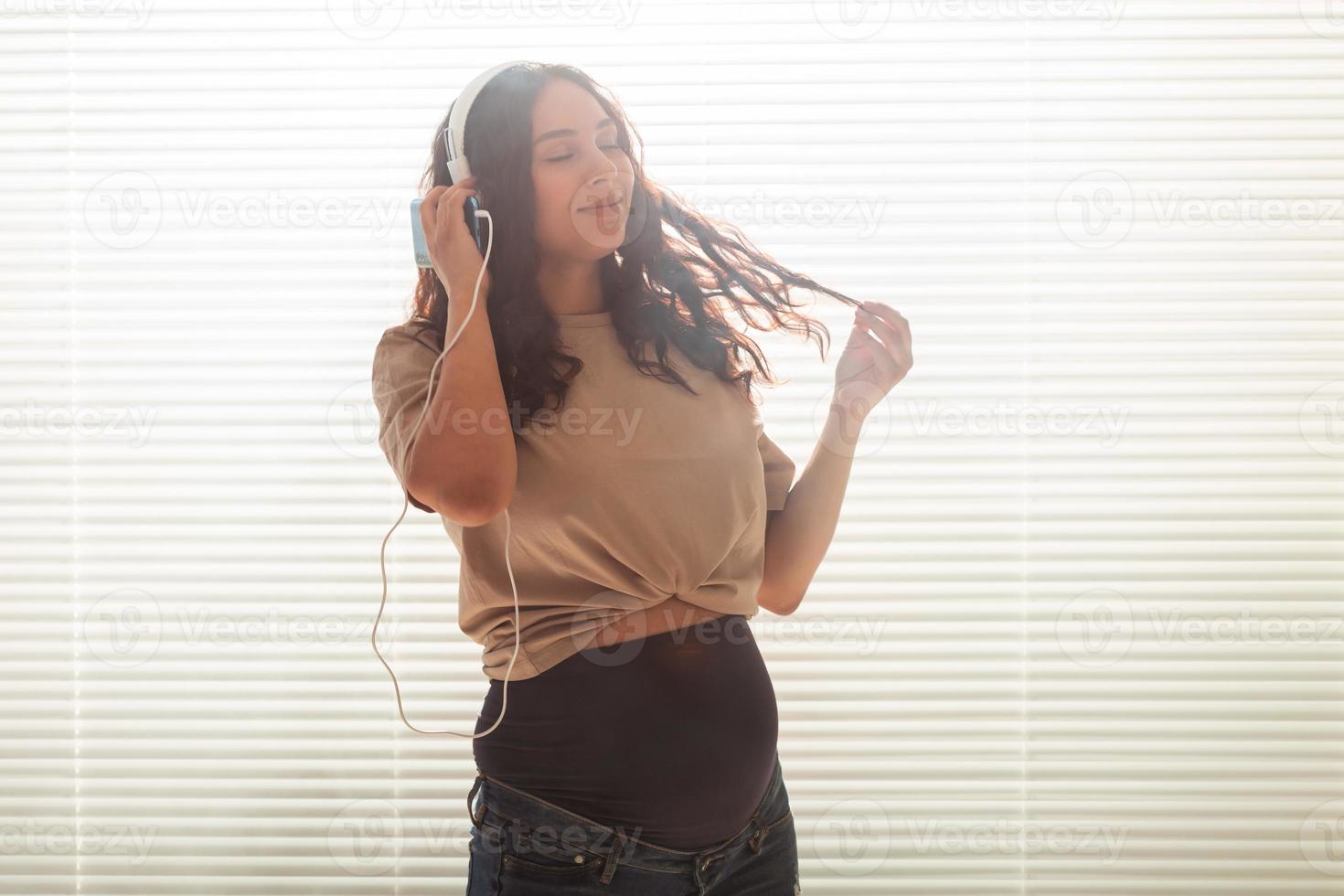 mujer embarazada escucha música con auriculares en casa y baila, copia espacio. foto