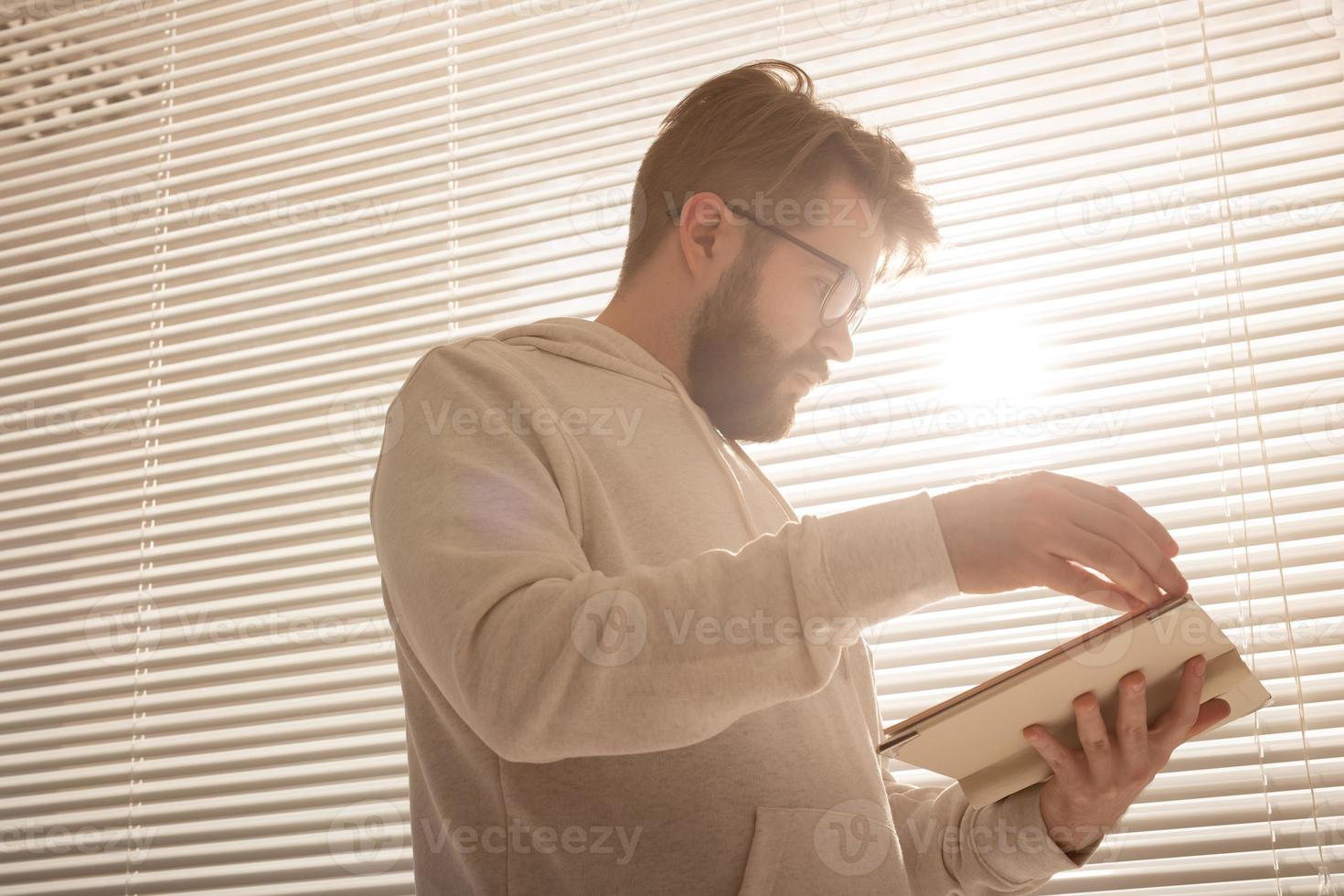 Bottom view of pensive stylish hipster man leafing through his daily planner in front of the blinds. Planning and time saving concept photo