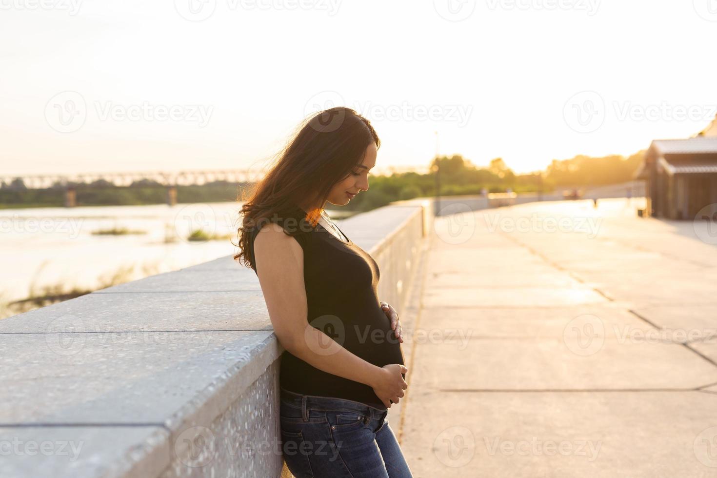mujer hispana embarazada en el terraplén, tocando el vientre. espacio de copia. foto