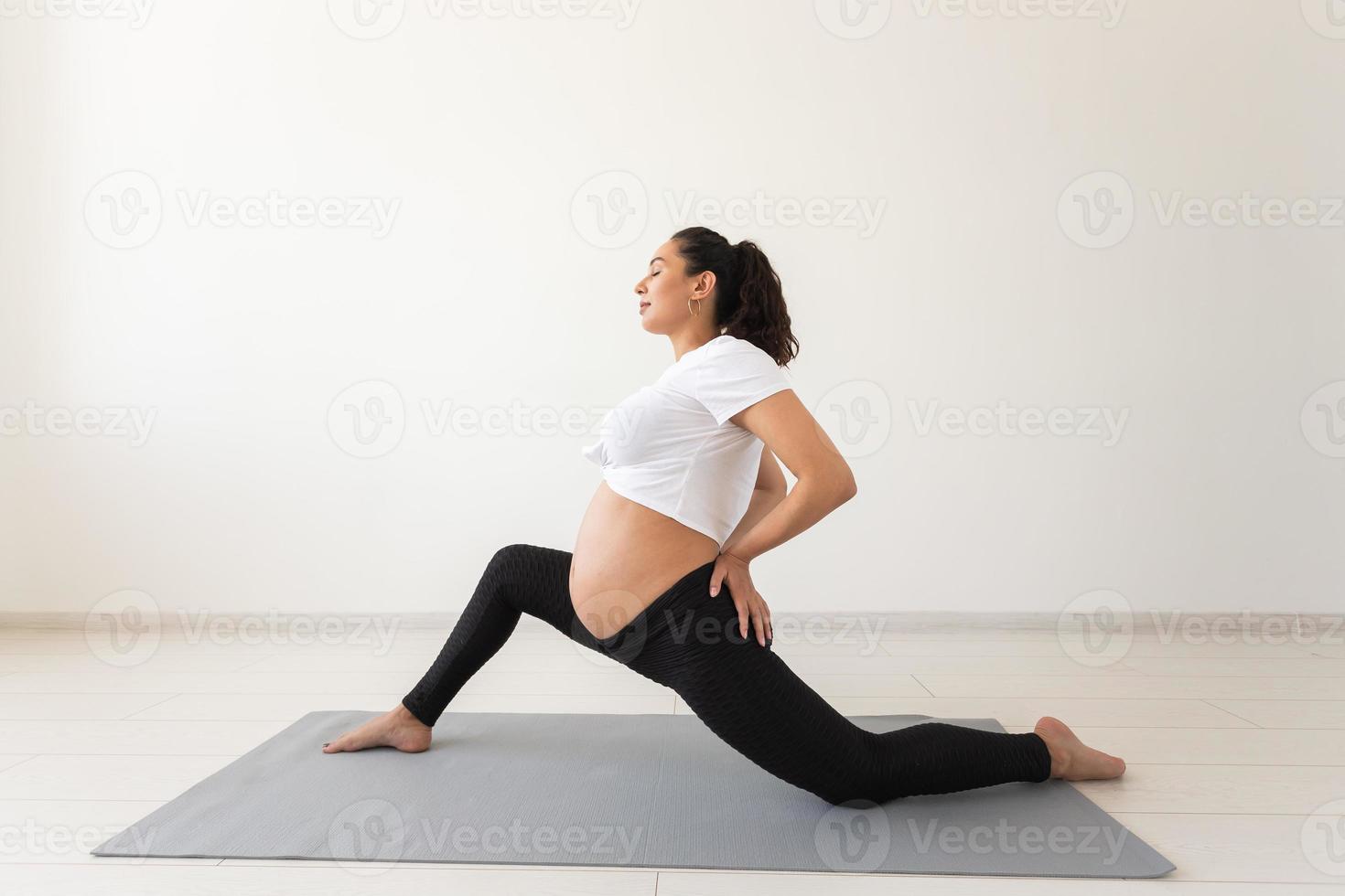 Young flexible pregnant woman doing gymnastics on rug on the floor on white background. The concept of preparing the body for easy childbirth photo