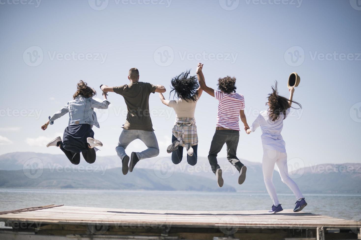 retrato de jóvenes amigos saltando del embarcadero al lago. amigos en el aire en un día soleado en el lago. foto