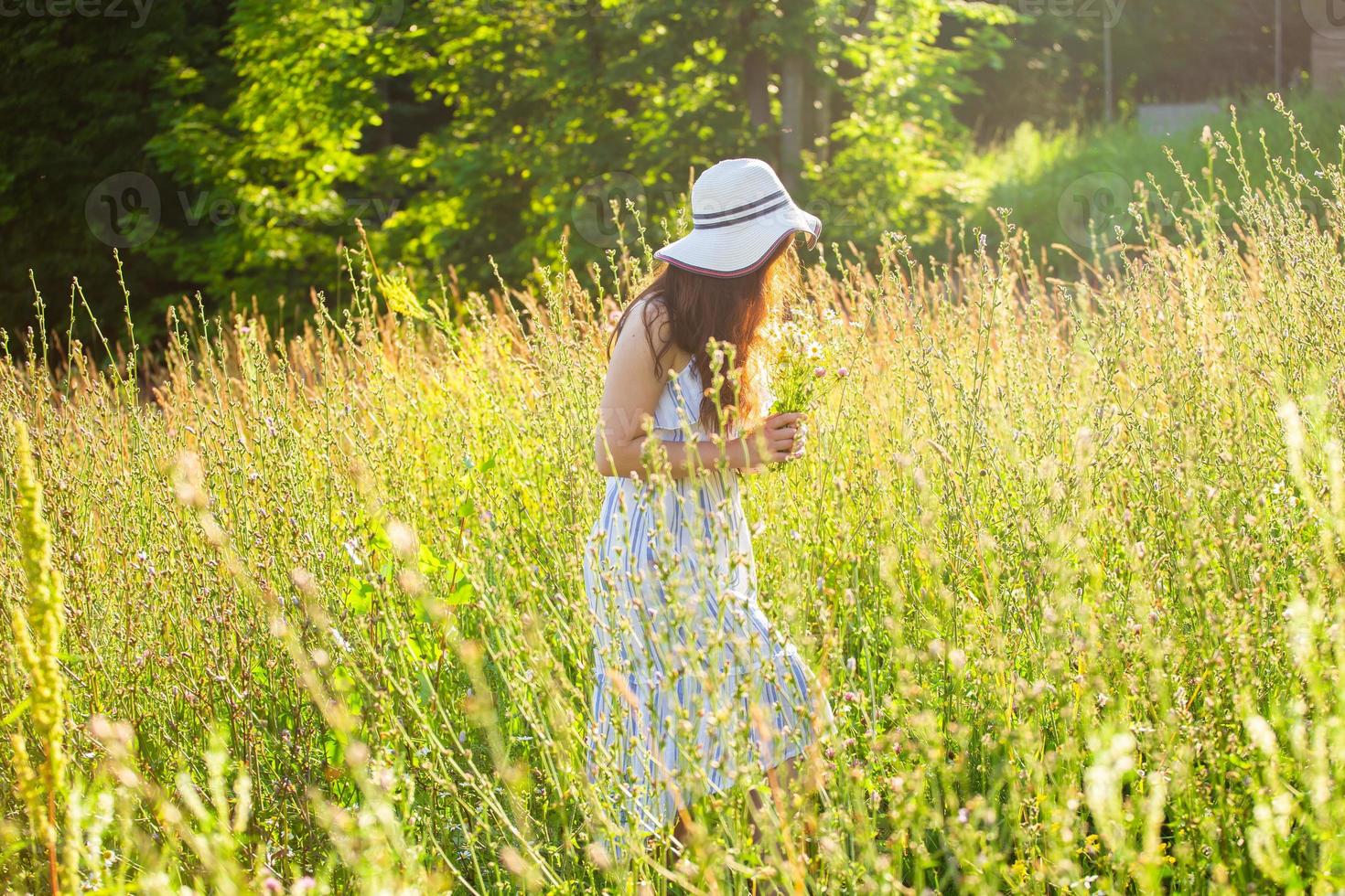 Happy young woman with long hair in hat and dress walking through the summer forest on a sunny day. Summer joy concept photo