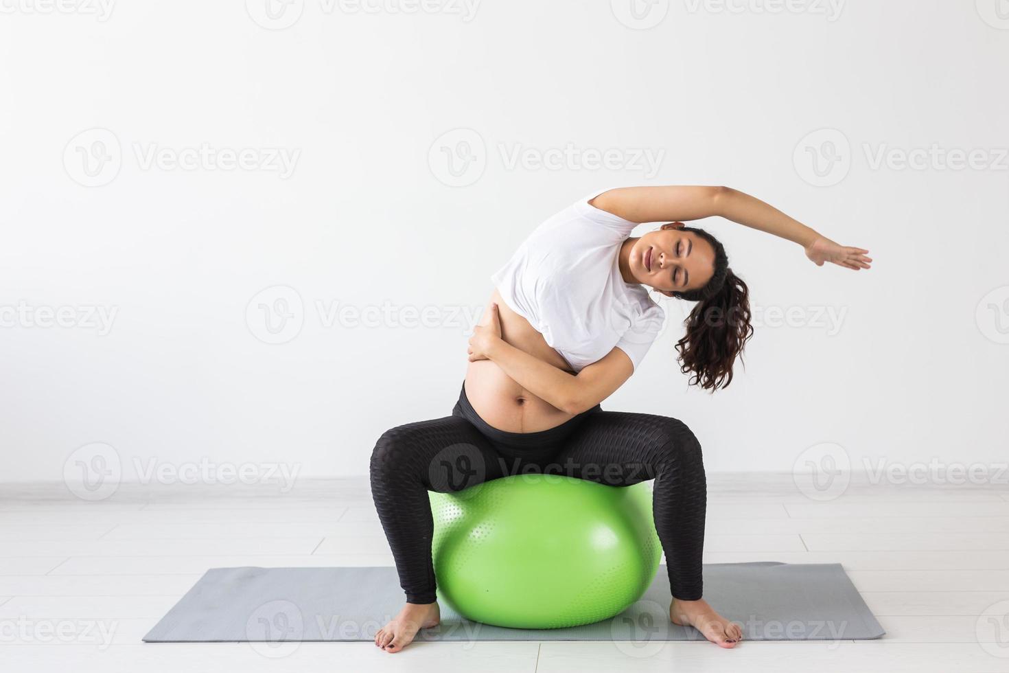 Young flexible pregnant woman doing gymnastics on rug on the floor on white background. The concept of preparing the body for easy childbirth photo