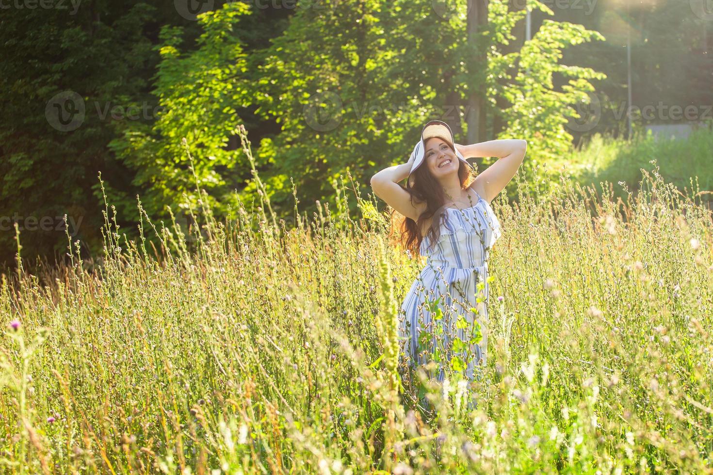 Happy young woman with long hair in hat and dress walking through the summer forest on a sunny day. Summer joy concept photo