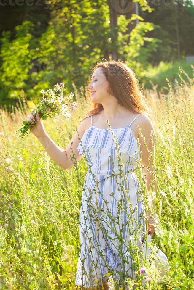 mujer joven caminando entre flores silvestres en un día soleado de verano. concepto de la alegría de comunicarse con la naturaleza de verano foto